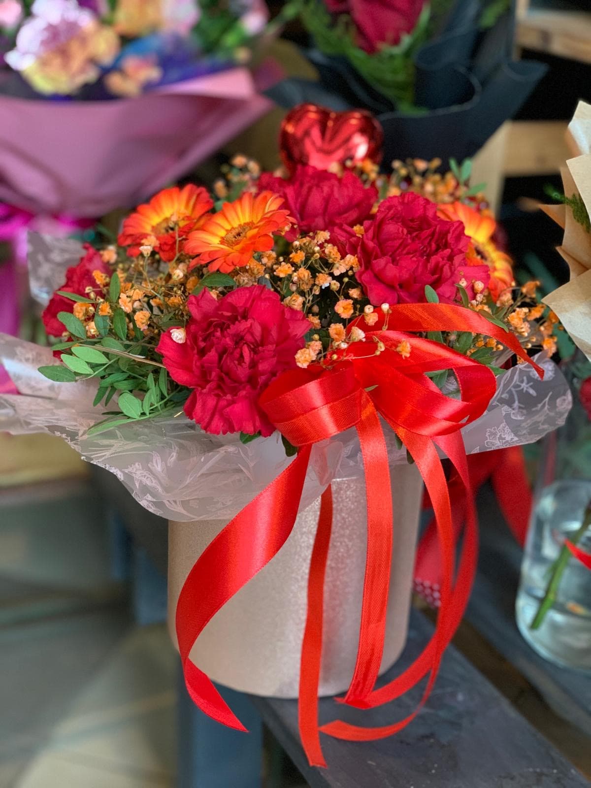 Flowerbox z czerwonymi goździkami, pomarańczowymi gerberami i czerwoną kokardą - kwiaty w pudełku Lębork